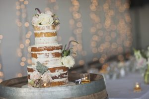 Naked wedding cake with roses on a rustic barrel