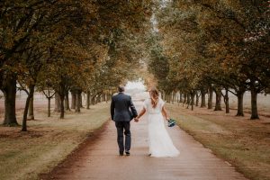 Bride and Groom hand in hand walking down a tree lined path